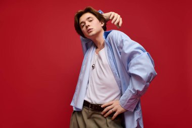 Genç bir adam şık bir pantolon ve mavi gömlekle rahatça poz verir.