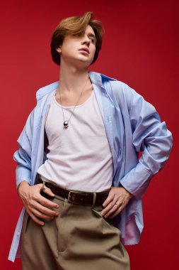 Genç adam kendine güveni tam bir poz veriyor. Üzerinde pantolon ve mavi gömlek var.