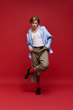 Modaya uygun genç bir adam, kendine güvenen bir pozla şık bir elbise, mavi gömlek ve pantolon giyer..