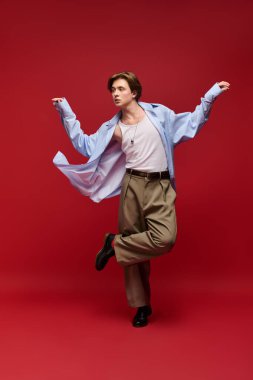 Genç bir adam modaya uygun giysiler içinde şık mavi gömleğini ve pantolonunu göstererek poz veriyor..