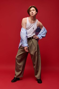 Genç bir adam şık bir şekilde şık bir pantolon ve kolsuz gömlekle poz veriyor..