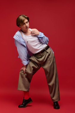 Şık bir genç adam, modaya uygun bir atlet ve pantolonun içinde kırmızı bir zemine karşı güvenle poz verir..