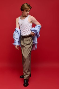 Genç bir adam kendine güvenerek şık bir elbise içinde poz veriyor, kolsuz bluz ve pantolonu var..