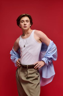 Genç adam kendine güvenen bir şekilde şık bir bluz ve canlı kırmızı arka planda şık bir pantolon giyiyor..