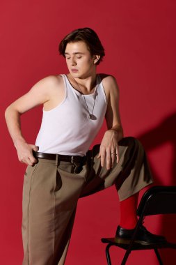 Genç adam kendine güveni tam bir şekilde poz veriyor, kırmızı arka planda modern modanın altını çiziyor..