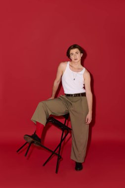 Şık bir genç adam kendine güvenen bir şekilde poz verir, kolsuz bluz ve pantolon giyer..