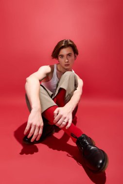 Şık bir genç adam canlı kırmızı bir arka plana karşı şık bir elbiseyle güven içinde poz verir..