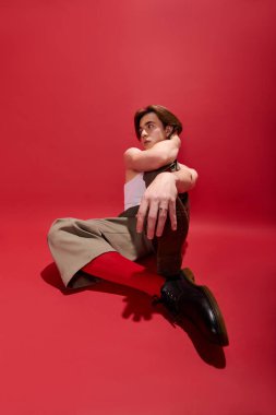 Modaya uygun genç bir adam tarzını ifade eder. Kolsuz bluz ve pantolon giyer, poz verir..