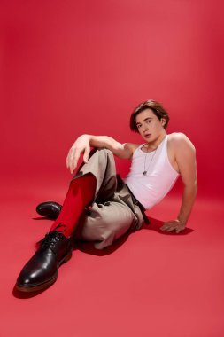 Şık bir genç adam şık bir atlet ve şık bir pantolon içinde koyu kırmızı bir arka planda dinleniyor..