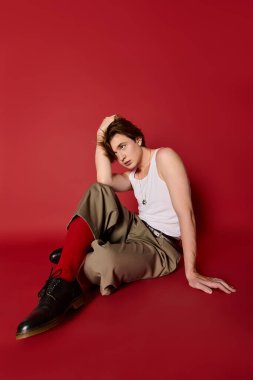 Şık bir genç adam, kırmızı arka planda kendine güvenen bir bluz ve şık bir pantolon giyer..