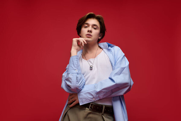 Уверенный молодой человек демонстрирует модные брюки и синие рубашки стиль с ярким красным фоном.