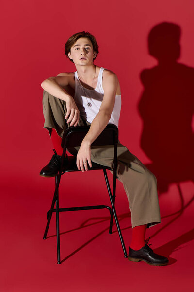 Стильный молодой человек уверенно позирует в майке танка на ярком красном фоне.