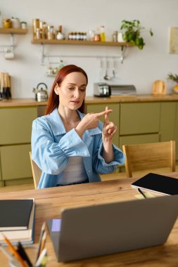 A red-haired woman teaches language remotely, using her laptop while sitting at a kitchen table.