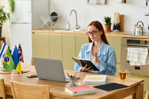 A woman with red hair teaches language online using her laptop while sitting at a home table.