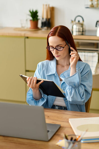 A woman with red hair teaches languages from her home, focused on her laptop and notes.