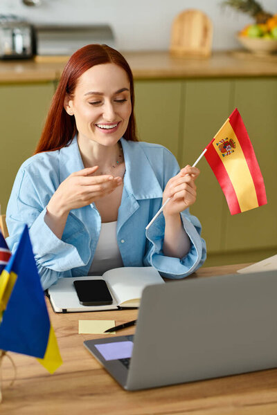 A woman with red hair teaches Spanish online, holding a flag while connecting with her students.