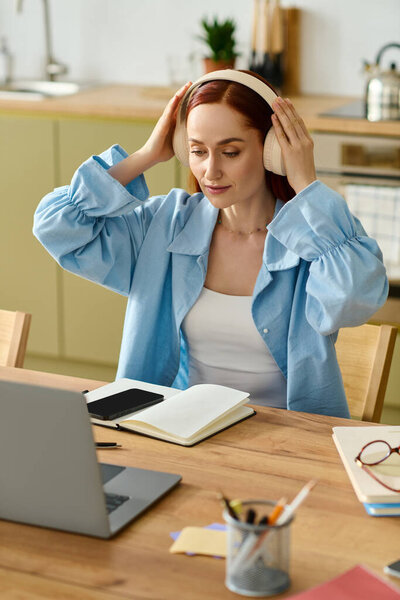 A woman with red hair teaches a language class online using her laptop in a cozy home setting.