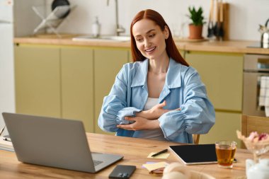 A language teacher with red hair is guiding students online from her home office, using her laptop.