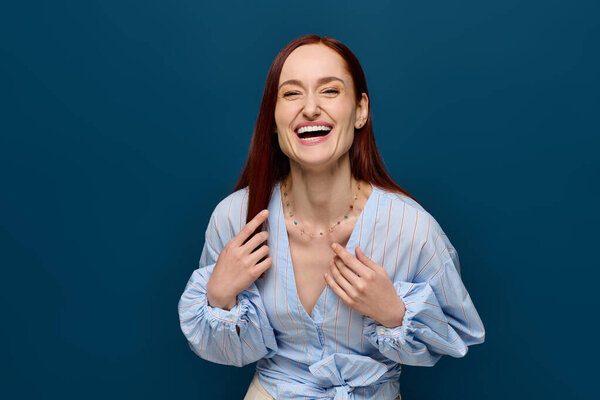 A woman with striking red hair beams with happiness while wearing a light blue blouse.