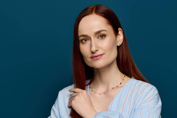 A woman with vibrant red hair poses gracefully, dressed in a blouse, radiating confidence.