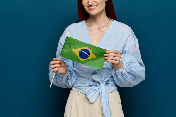 A woman with vibrant red hair is holding a Brazilian flag in a colorful studio setting.