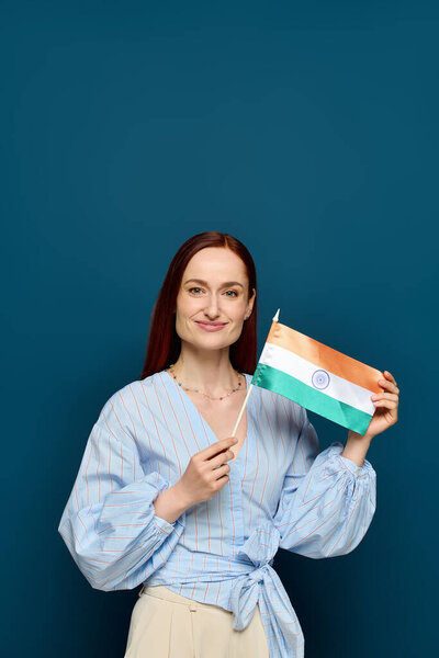 A dynamic language teacher with striking red hair is holding a flag, celebrating culture.