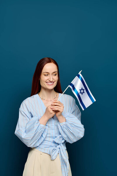 A language teacher with red hair smiles while holding a flag in her studio space.