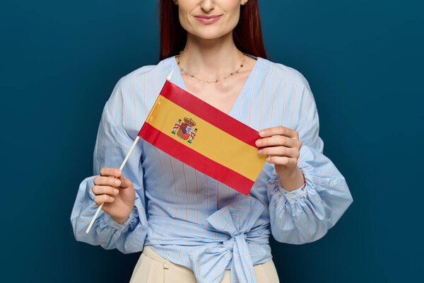 A woman with red hair teaches language while proudly displaying a Spanish flag in her studio.