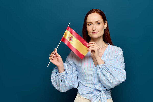 Language teacher with red hair holds the Spanish flag against a blue background, highlighting pride.