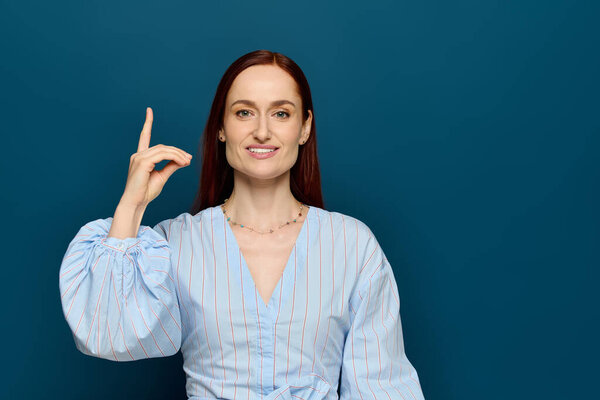A woman with red hair teaches sign language against a blue background, showcasing her skills.