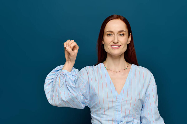 A red-haired woman teaches sign language, smiling in front of a blue background.