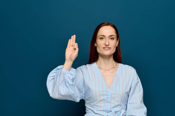 A woman with red hair demonstrates sign language while teaching a class in a bright setting.
