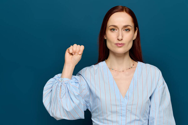 A woman with red hair teaches sign language, demonstrating a gesture against a blue background.
