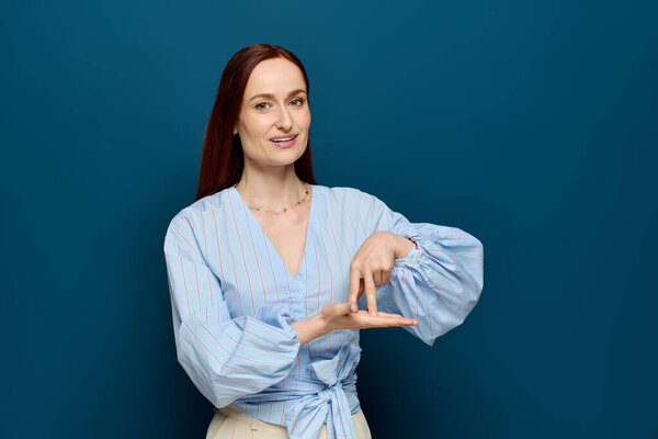 A smiling woman with red hair teaches sign language against a blue background.
