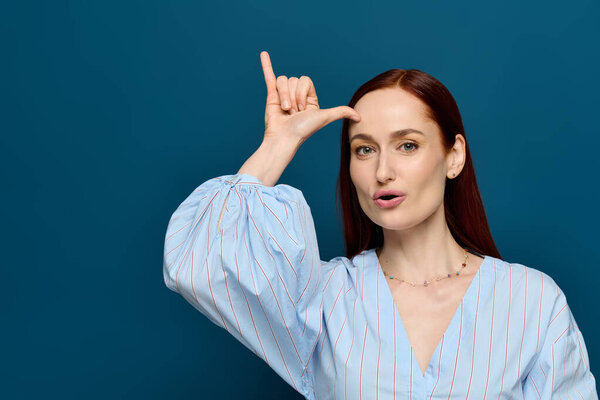 A woman with red hair teaches sign language in front of a blue background during her class.