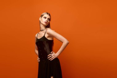 Güzel genç bayan, parlak turuncu duvara karşı, Cadılar Bayramı kostümü içinde güven içinde poz veriyor..