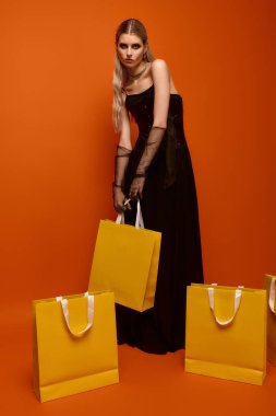 Göz kamaştırıcı bir Cadılar Bayramı kostümü giymiş genç bir kadın sarı alışveriş torbalarıyla poz veriyor..