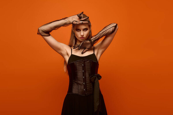 A young woman showcases her Halloween costume, striking a confident pose against an orange backdrop.