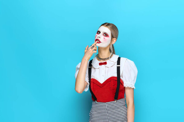 A beautiful young woman poses confidently in her Halloween costume against a vibrant blue backdrop.