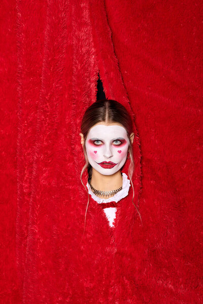 A young woman peeks from a red curtain, revealing a creative Halloween look.