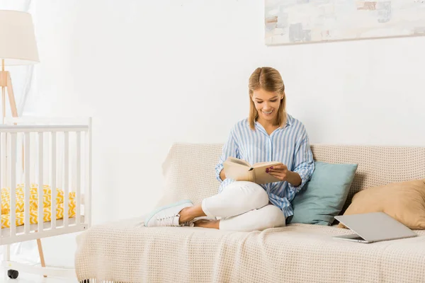 Femme adulte souriante assise sur le canapé livre de lecture — Photo de stock