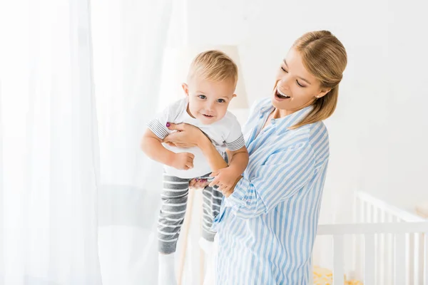 Веселая мать держит малыша в руках в детской комнате — стоковое фото