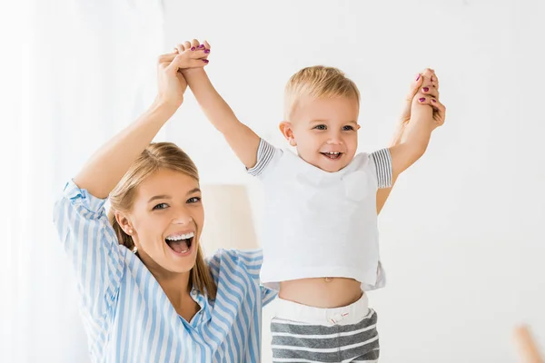 Allegra madre guardando la fotocamera e tenendo sorridente bambino in mano — Foto stock