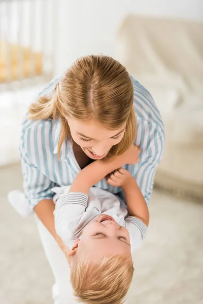 Cheerful mother looking at toddler and holding him in hands — Stock Photo