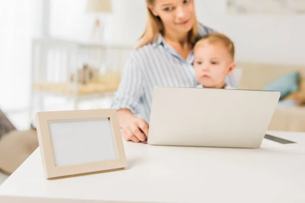 Мать сидит за столом с милым малышом при использовании ноутбука, сосредоточиться на переднем плане — стоковое фото