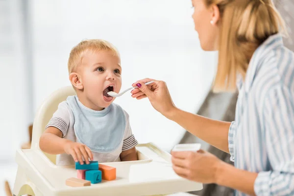 Mother feeding son in highchair with baby food — Stock Photo