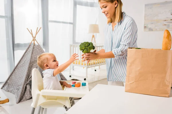 Mother giving son sitting in baby chair broccoli — Stock Photo