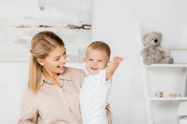 Весела мати тримає усміхненого сина в дитячій кімнаті — стокове фото