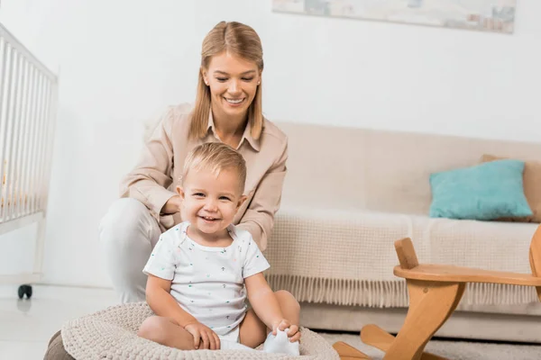 Smiling mother and adorable toddler looking at camera sitting in nursery room — Stock Photo
