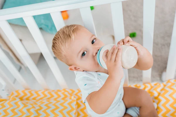 Entzückendes Kleinkind trinkt aus Babyflasche im Kinderbett — Stockfoto